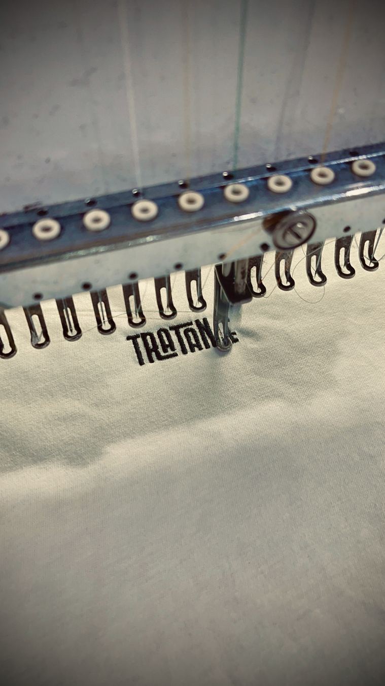 Máquina de bordar a bordar o logo TRATANTE numa t-shirt branca